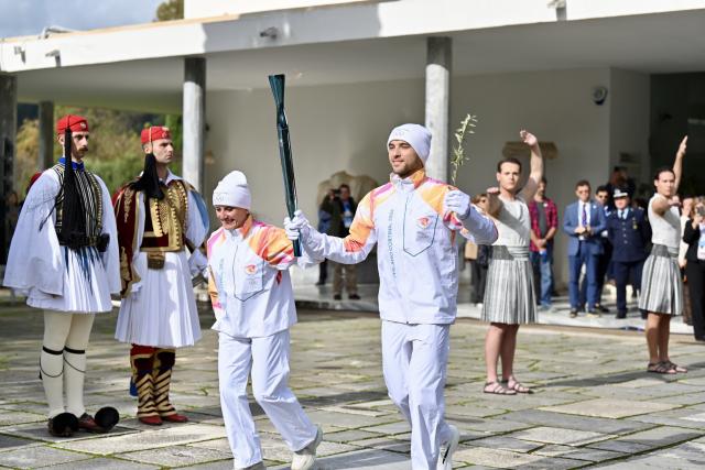 (251126) -- ANCIENT OLYMPIA, Nov. 26, 2025 (Xinhua) -- The first torchbearer, Greek rower Petros Gkaidatzis (R, front) and second torchbearer, Italian former cross-country skier Stefania Belmondo (L, front) carry the torch during the torch relay after the Olympic flame lighting ceremony for the Milan-Cortina 2026 Winter Olympic Games in Ancient Olympia, Greece, on Nov. 26, 2025. (Xinhua/Lyu You)