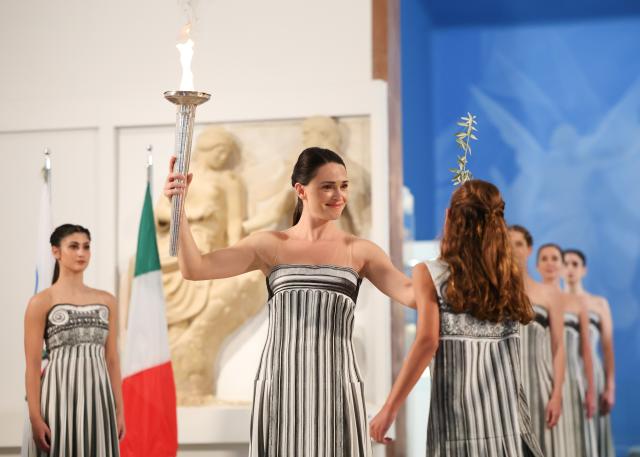 (251126) -- ANCIENT OLYMPIA, Nov. 26, 2025 (Xinhua) -- Actress Mary Mina (2nd L), in the role of an ancient Greek High Priestess, carries the flame and an olive branch during the Olympic flame lighting ceremony for the Milan-Cortina 2026 Winter Olympic Games in Ancient Olympia, Greece, on Nov. 26, 2025. (Xinhua/Li Jing)
