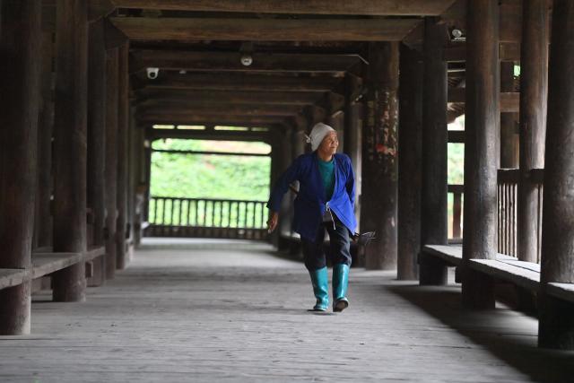 (251127) -- NANNING, Nov. 27, 2025 (Xinhua) -- An old woman walks past a timber lounge bridge in Batuan Village in Sanjiang Dong Autonomous County, south China's Guangxi Zhuang Autonomous Region, Nov. 5, 2025. Mountains, gullies and streams surrounding the villages across Guangxi's rural area make bridges the must for production and daily life. Small bridges are not only important transportation link, but also play a crucial role in culture inheritance, industrial development and rural revitalization. (Xinhua/Huang Xiaobang)
