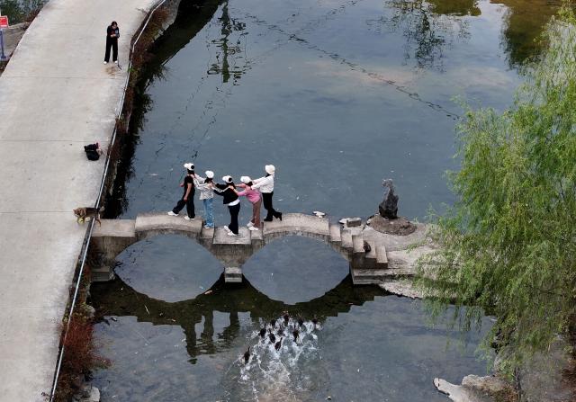(251127) -- NANNING, Nov. 27, 2025 (Xinhua) -- An aerial drone photo taken on Nov. 1, 2025 shows tourists posing for photos on a small bridge in a village of Jinde Town in Liuzhou City, south China's Guangxi Zhuang Autonomous Region. Mountains, gullies and streams surrounding the villages across Guangxi's rural area make bridges the must for production and daily life. Small bridges are not only important transportation link, but also play a crucial role in culture inheritance, industrial development and rural revitalization. (Xinhua/Huang Xiaobang)
