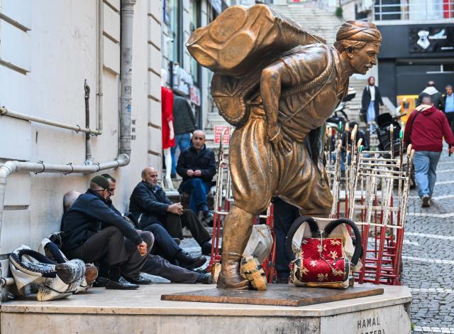 (251201) -- ISTANBUL, Dec. 1, 2025 (Xinhua) -- Porters rest next to a statue of a porter in the Eminonu commercial district of Istanbul, Türkiye, Nov. 25, 2025. In the old quarters of Istanbul, one often encounters a familiar scene: men weaving through narrow streets, carrying heavy loads on their backs or pushing them on handcarts. Known in Turkish as "hamal," these traditional porters represent a profession that dates back to the Ottoman era and endures to this day.
   The porters'tools are simple -- a thick shoulder strap or a sturdy handcart. Dozens of kilograms, sometimes even loads exceeding a hundred kilograms, are lifted and transported with steady precision before disappearing into the maze-like streets.
   The Grand Bazaar, the Spice Bazaar, and the commercial district of Eminonu are among Istanbul's oldest and busiest trading hubs. Dense shopfronts, heavy foot traffic, and a network of narrow alleys and intersections leave little room for motor vehicles, which have allowed the hamal profession to survive and remain indispensable.
   In these labyrinthine streets, they shoulder countless small-scale logistics tasks, quietly sustaining the commercial lifeblood of the city. In Istanbul, being a porter is not only a traditional craft -- it is a foundational force that has supported the city's commercial vitality for centuries. (Xinhua/Liu Lei)
