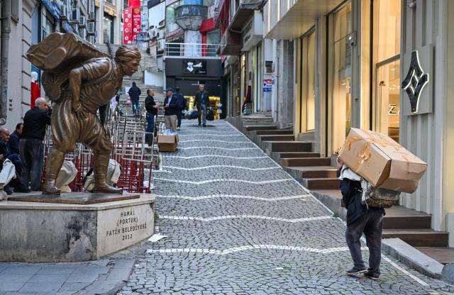 (251201) -- ISTANBUL, Dec. 1, 2025 (Xinhua) -- A porter carries goods past a statue of a porter in the Eminonu commercial district of Istanbul, Türkiye, Nov. 6, 2025. In the old quarters of Istanbul, one often encounters a familiar scene: men weaving through narrow streets, carrying heavy loads on their backs or pushing them on handcarts. Known in Turkish as "hamal," these traditional porters represent a profession that dates back to the Ottoman era and endures to this day.
   The porters'tools are simple -- a thick shoulder strap or a sturdy handcart. Dozens of kilograms, sometimes even loads exceeding a hundred kilograms, are lifted and transported with steady precision before disappearing into the maze-like streets.
   The Grand Bazaar, the Spice Bazaar, and the commercial district of Eminonu are among Istanbul's oldest and busiest trading hubs. Dense shopfronts, heavy foot traffic, and a network of narrow alleys and intersections leave little room for motor vehicles, which have allowed the hamal profession to survive and remain indispensable.
   In these labyrinthine streets, they shoulder countless small-scale logistics tasks, quietly sustaining the commercial lifeblood of the city. In Istanbul, being a porter is not only a traditional craft -- it is a foundational force that has supported the city's commercial vitality for centuries. (Xinhua/Liu Lei)