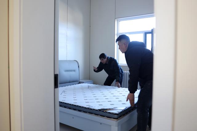 (251202) -- YUZHONG, Dec. 2, 2025 (Xinhua) -- Villagers lay down a mattress at their new home at a resettlement site for flood affected households in Jiuzhuanggou Village of Mapo Town in Yuzhong County, northwest China's Gansu Province, Dec. 1, 2025. Yuzhong County, which is under the jurisdiction of the provincial capital Lanzhou, was hit by mountain torrents triggered by torrential rains this August. According to a reconstruction plan made by the local government, six resettlement sites for 325 families are on construction smoothly. 
Currently, the supporting facilities as well as indoor and outdoor decorations at these resettlement sites are almost finished, waiting for check upon delivery. Disaster-affected people are moving into new homes in batches. (Xinhua/Chen Bin)