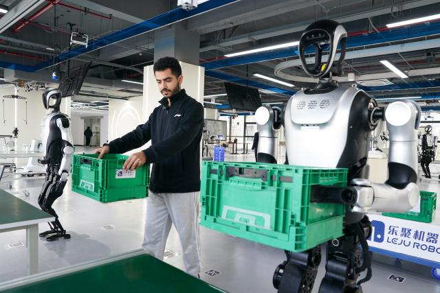 (251202) -- HEFEI, Dec. 2, 2025 (Xinhua) -- Ahmed Medhat Mostafa Elsayed carries goods with a robot at the pre-training venue for the Embodied Artificial Intelligence (EAI) robots data collection in Hefei, east China's Anhui Province, Nov. 28, 2025. The 23-year-old Ahmed Medhat Mostafa Elsayed is an Egyptian student who is currently doing research in particle physics at the University of Science and Technology of China in Hefei.
    Elsayed came to China at the age of ten in 2012. Influenced by his father, who works in the physics area, Elsayed gradually developed a strong interest in physics. After graduating from Sichuan University of Science and Engineering with a bachelor's degree in physics two years ago, he entered the University of Science and Technology of China for his postgraduate study. 
    Now Elsayed, whose research topic focuses on heavy neutrinos, plans to apply for the doctoral degree here, hoping he could make some influential scientific research achievements in the future and  could become a bridge on academic exchange between China and the world. (Xinhua/Du Yu)