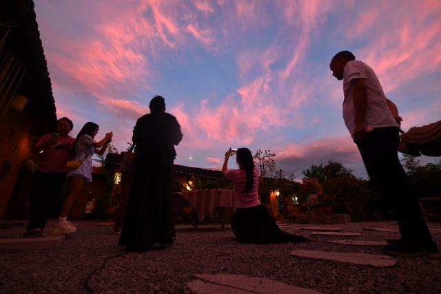 (251203) -- LIUZHOU, Dec. 3, 2025 (Xinhua) -- Tourists take photos during the twilight at Jilong Village, in Liujiang District, Liuzhou City, south China's Guangxi Zhuang Autonomous Region, Oct. 5, 2025. In recent years, Liujiang District of Liuzhou City has leveraged its thriving rural industries and vibrant agricultural economy to expand its tourism business. In the first three quarters of this year, Liujiang District received a total of 5.9975 million visits, a year-on-year increase of 11.16 percent, with tourism-related revenue of 6.006 billion yuan (850.26 million U.S. dollars), up 9.91 percent compared to the same period last year. (Xinhua/Huang Xiaobang)