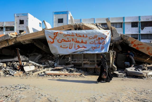 (251203) -- GAZA, Dec. 3, 2025 (Xinhua) -- A Palestinian women walks by the abandoned Israeli army vehicle which is now a charging station, in Gaza City, on Nov. 30, 2025. TO GO WITH "Feature: From army vehicle to power source -- a Gazan's retooling of war" (Photo by Rizek Abdeljawad/Xinhua)