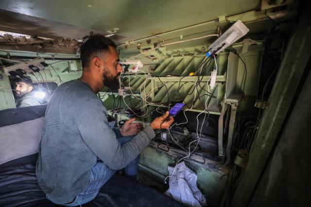 (251204) -- BEIJING, Dec. 4, 2025 (Xinhua) -- Palestinian men use power facilities inside the abandoned Israeli army vehicle, in Gaza City, on Nov. 30, 2025. (Photo by Rizek Abdeljawad/Xinhua)