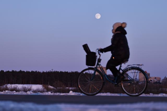 (251204) -- BEIJING, Dec. 4, 2025 (Xinhua) -- A citizen cycles as a full moon is seen over Tongjiang City, northeast China's Heilongjiang Province, Dec. 4, 2025. This year's second-largest full moon to the eyes of lunar observers will appear on Friday morning, but the best viewing time falls on Thursday evening. (Photo by Liu Wanping/Xinhua)