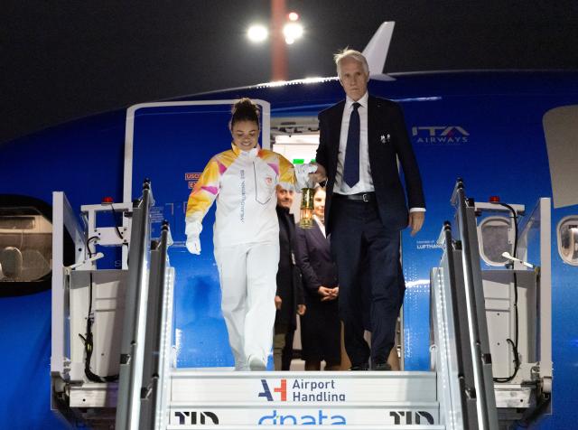 (251205) -- ROME, Dec. 5, 2025 (Xinhua) -- Italy's tennis player and Olympic champion Jasmine Paolini (L) and Giovanni Malago, president of the Milan-Cortina organizing committee, walk down the gangway with a lantern holding the flame of 2026 Milan-Cortina Olympic Winter Games at Fiumicino Airport in Rome, Italy, Dec. 4, 2025. The Olympic flame for the 2026 Winter Games arrived in Rome, Italy on Thursday afternoon, marking the start of a series of torch relay events. (Xinhua/Li Jing)