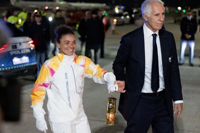(251205) -- ROME, Dec. 5, 2025 (Xinhua) -- Italy's tennis player and Olympic champion Jasmine Paolini (L) and Giovanni Malago, president of the Milan-Cortina organizing committee, walk down the gangway with a lantern holding the flame of 2026 Milan-Cortina Olympic Winter Games at Fiumicino Airport in Rome, Italy, Dec. 4, 2025. The Olympic flame for the 2026 Winter Games arrived in Rome, Italy on Thursday afternoon, marking the start of a series of torch relay events. (Xinhua/Li Jing)