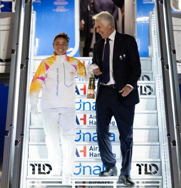 (251205) -- ROME, Dec. 5, 2025 (Xinhua) -- Italy's tennis player and Olympic champion Jasmine Paolini (L) and Giovanni Malago, president of the Milan-Cortina organizing committee, walk down the gangway with a lantern holding the flame of 2026 Milan-Cortina Olympic Winter Games at Fiumicino Airport in Rome, Italy, Dec. 4, 2025. The Olympic flame for the 2026 Winter Games arrived in Rome, Italy on Thursday afternoon, marking the start of a series of torch relay events. (Xinhua/Li Jing)