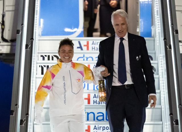 (251205) -- ROME, Dec. 5, 2025 (Xinhua) -- Italy's tennis player and Olympic champion Jasmine Paolini (L) and Giovanni Malago, president of the Milan-Cortina organizing committee, walk down the gangway with a lantern holding the flame of 2026 Milan-Cortina Olympic Winter Games at Fiumicino Airport in Rome, Italy, Dec. 4, 2025. The Olympic flame for the 2026 Winter Games arrived in Rome, Italy on Thursday afternoon, marking the start of a series of torch relay events. (Xinhua/Li Jing)