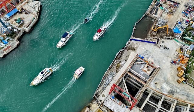 (251205) -- SANYA, Dec. 5, 2025 (Xinhua) -- Yachts are seen in waters over the Sanya River estuary passage project in Sanya, south China's Hainan Province, Dec. 5, 2025. The Sanya River estuary passage project undertaken by China Railway 20th Bureau Group was successfully drilled through on Friday. This 3.118-kilometer underwater tunnel, the first of its kind in Sanya, is expected to further optimize the urban spatial layout of the city, and facilitate the development of the Hainan Free Trade Port. (Xinhua/Zhao Yingquan)