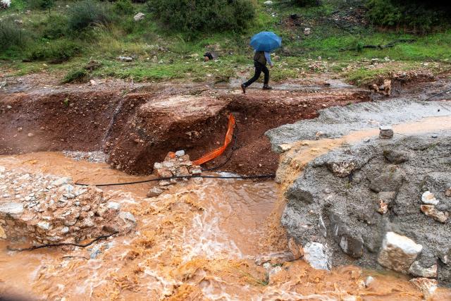 (251205) -- MANDRA, Dec. 5, 2025 (Xinhua) -- A resident walks by a road blocked by a landslide in Mandra, in western Attica, about 20 kilometers west of central Athens, Greece, Dec. 5, 2025. A powerful storm, named Byron by local meteorologists, continued to batter Greece for a second consecutive day on Friday, triggering widespread flooding. (Photo by Marios Lolos/Xinhua)