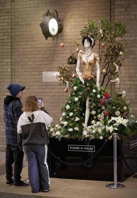 (251206) -- VANCOUVER, Dec. 6, 2025 (Xinhua) -- People view a floral mannequin displayed on the street during the Fleurs de Villes NOËL event in Vancouver, British Columbia, Canada, on Dec. 5, 2025. Featuring 30 stunning floral installations created by local floral artists to celebrate the holiday season, this annual event exhibition kicked off here on Friday and will run until December 14. (Photo by Liang Sen/Xinhua)