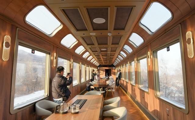 (251206) -- HARBIN, Dec. 6, 2025 (Xinhua) -- People take photos in a carriage of a tourist train dubbed Yichun, in northeast China's Heilongjiang Province, Dec. 6, 2025. A tourist train dubbed Yichun began trial operation on Saturday. More than 40 invited passengers boarded the train at Harbin Railway Station for a trip bound to Yabuli Ski Resort. The train features five themed carriages and offers live band and traditional folk performances for passengers. (Xinhua/Wang Song)