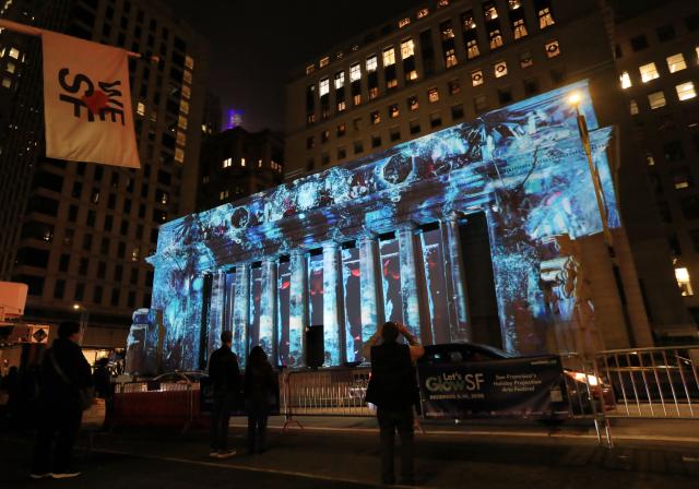 (251206) -- SAN FRANCISCO, Dec. 6, 2025 (Xinhua) -- People watch a light projection on the wall of a building in San Francisco, the United States, Dec. 5, 2025. "Let's Glow SF", a holiday projection arts event, started here on Friday night. Large-scale art projection works will be displayed on the facades of eight iconic buildings in downtown San Francisco from the night of Dec. 5 to 14. (Photo by Liu Yilin/Xinhua)