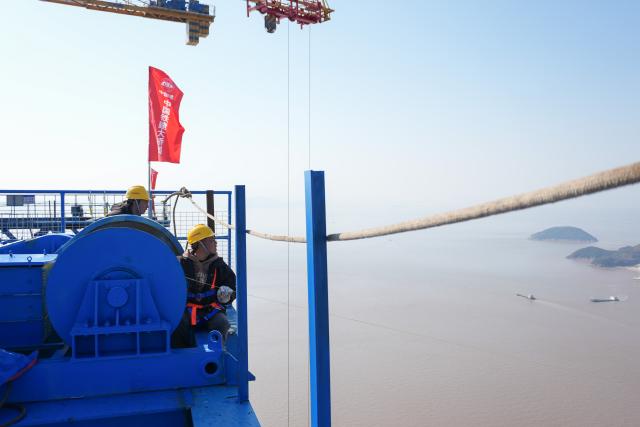(251206) -- ZHOUSHAN, Dec. 6, 2025 (Xinhua) -- Workers install pilot cables for the Shuangyumen super major bridge in east China's Zhejiang Province, Dec. 6, 2025. The pilot cable installation for the Shuangyumen super major bridge, part of the second phase of the Liuheng Highway Bridge project at Ningbo-Zhoushan Port in Zhejiang Province, completed successfully on Saturday. This marks the official commencement of the catway construction on the bridge.
   The project consists of two sea-crossing bridges - Shuangyumen super major bridge and Qinglongmen super major bridge, as well as connection lines between them. Upon completion, the project will further improve the integrated land-sea transportation network of Ningbo-Zhoushan Port. (Xinhua/Huang Zongzhi)
