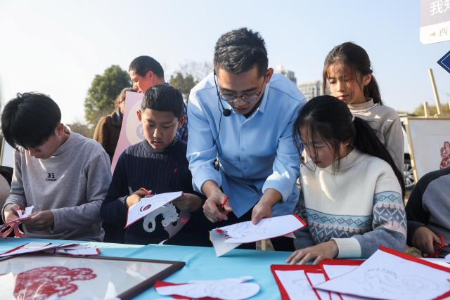 (251207) -- JIANDE, Dec. 7, 2025 (Xinhua) -- A staff member (C) guides students to experience paper-cutting at a farmers' fair in Qiantan Town of Jiande City, east China's Zhejiang Province, Dec. 6, 2025. The farmers' fair kicked off here in Qiantan Town of Jiande City on Saturday. Over 300 stalls line up along a riverside walkway spanning nearly two kilometers, with a wide variety of daily necessities, agricultural products, local snacks, children's toys and more on display. 
   As the liveliest such event held at the end of the year in the area, the ongoing farmers' fair also features elements such as cultural performances and talent market. (Xinhua/Xu Yu)