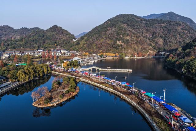(251207) -- JIANDE, Dec. 7, 2025 (Xinhua) -- An aerial drone photo taken on Dec. 6, 2025 shows a view of a farmers' fair in Qiantan Town of Jiande City, east China's Zhejiang Province. The farmers' fair kicked off here in Qiantan Town of Jiande City on Saturday. Over 300 stalls line up along a riverside walkway spanning nearly two kilometers, with a wide variety of daily necessities, agricultural products, local snacks, children's toys and more on display. 
   As the liveliest such event held at the end of the year in the area, the ongoing farmers' fair also features elements such as cultural performances and talent market. (Xinhua/Xu Yu)
