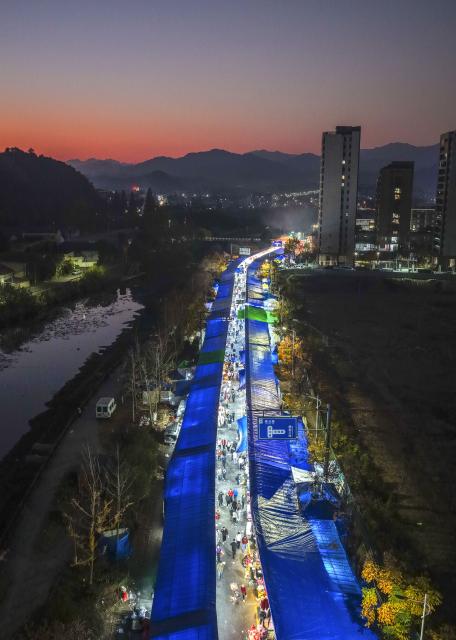 (251207) -- JIANDE, Dec. 7, 2025 (Xinhua) -- An aerial drone photo taken on Dec. 6, 2025 shows a view of a farmers' fair in Qiantan Town of Jiande City, east China's Zhejiang Province. The farmers' fair kicked off here in Qiantan Town of Jiande City on Saturday. Over 300 stalls line up along a riverside walkway spanning nearly two kilometers, with a wide variety of daily necessities, agricultural products, local snacks, children's toys and more on display. 
   As the liveliest such event held at the end of the year in the area, the ongoing farmers' fair also features elements such as cultural performances and talent market. (Xinhua/Xu Yu)