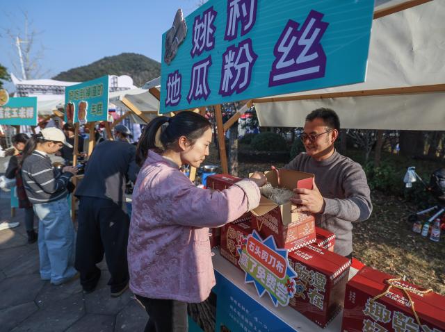 (251207) -- JIANDE, Dec. 7, 2025 (Xinhua) -- Village cadre Huang Jianzhen (1st R) promotes sweet potato vermicelli to a customer at a farmers' fair in Qiantan Town of Jiande City, east China's Zhejiang Province, Dec. 6, 2025. The farmers' fair kicked off here in Qiantan Town of Jiande City on Saturday. Over 300 stalls line up along a riverside walkway spanning nearly two kilometers, with a wide variety of daily necessities, agricultural products, local snacks, children's toys and more on display. 
   As the liveliest such event held at the end of the year in the area, the ongoing farmers' fair also features elements such as cultural performances and talent market. (Xinhua/Xu Yu)