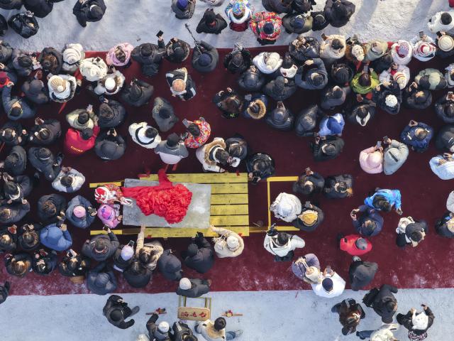 (251207) -- HARBIN, Dec. 7, 2025 (Xinhua) -- An aerial drone photo shows people viewing the first ice cube collected during an ice collecting festival in Harbin, northeast China's Heilongjiang Province, Dec. 7, 2025. Marking the beginning of Harbin's ice collecting season, the sixth ice collecting festival kicked off here by the Songhua River on Sunday, attracting lots of people with ice collecting ceremony and folk custom experience activities. (Xinhua/Wang Song)