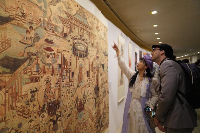 (251209) -- UNITED NATIONS, Dec. 9, 2025 (Xinhua) -- People visit an exhibition showcasing Tsinghua University's research and design work inspired by the ancient art of Dunhuang at the UN headquarters in New York, Dec. 8, 2025. More than 80 works are on display at the exhibition, from early masters such as Pang Xunqin, Chang Sha'na, Chen Hanmin and Liu Jude, to new pieces by Tsinghua students and alumni. (Xinhua/Zhang Fengguo)