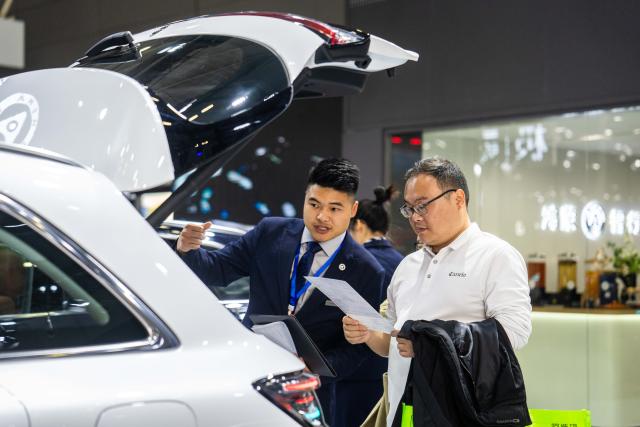 (251210) -- CHANGSHA, Dec. 10, 2025 (Xinhua) -- A staff member (L) introduces a car on display to a visitor at the 21st Changsha International Automobile Expo in Changsha, central China's Hunan Province, on Dec. 10, 2025. The 6-day expo kicked off on Wednesday at the Changsha International Convention and Exhibition Center, showcasing some 1,000 vehicles from over 70 automobile brands. (Xinhua/Chen Sihan)