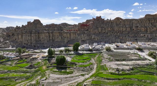(251210) -- LHASA, Dec. 10, 2025 (Xinhua) -- An aerial drone photo taken on June 24, 2025 shows the Piyang grottoes and a village below in Zanda County of Ngari Prefecture, southwest China's Xizang Autonomous Region. TO GO WITH "Feature: The mountains, the men, the murals: Guarding a lost kingdom on roof of the world" (Xinhua/Tenzin Nyida)