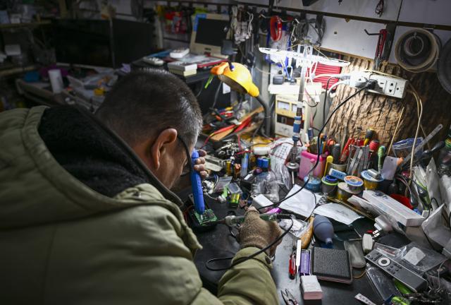(251210) -- TIANJIN, Dec. 10, 2025 (Xinhua) -- A technician repairs a home appliance at a shop in the "repair alley" in north China's Tianjin, Dec. 9, 2025. A "repair alley" established in June 2024 has become a lively hub for neighborhood-friendly repair services in Tianjin. In this dedicated zone, local residents have easy access to daily services such as knife sharpening, darning, locksmiths and watch repair. (Xinhua/Xu Jiayi)