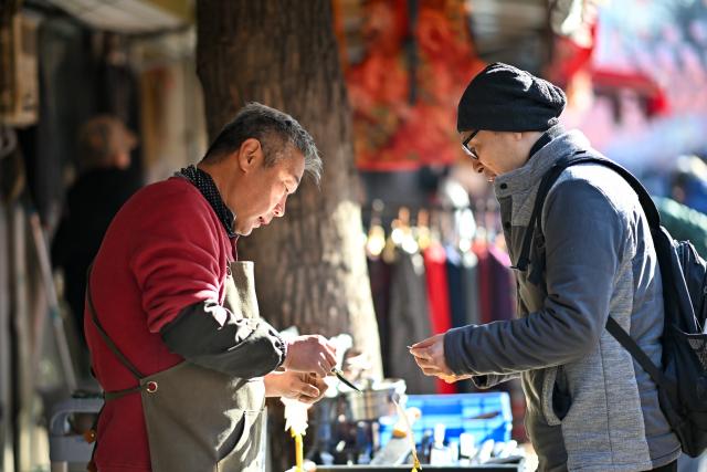 (251210) -- TIANJIN, Dec. 10, 2025 (Xinhua) -- A shopkeeper (L) introduces a knife to a customer at a shop in the "repair alley" in north China's Tianjin, Dec. 9, 2025. A "repair alley" established in June 2024 has become a lively hub for neighborhood-friendly repair services in Tianjin. In this dedicated zone, local residents have easy access to daily services such as knife sharpening, darning, locksmiths and watch repair. (Xinhua/Zhang Cheng)