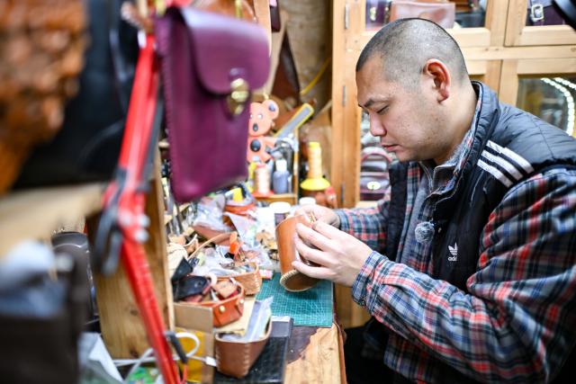 (251210) -- TIANJIN, Dec. 10, 2025 (Xinhua) -- A shopkeeper crafts leather goods at a shop in the "repair alley" in north China's Tianjin, Dec. 9, 2025. A "repair alley" established in June 2024 has become a lively hub for neighborhood-friendly repair services in Tianjin. In this dedicated zone, local residents have easy access to daily services such as knife sharpening, darning, locksmiths and watch repair. (Xinhua/Zhang Cheng)