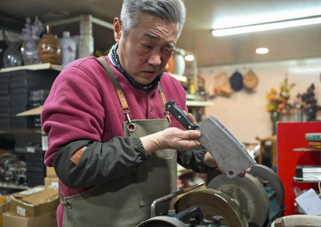 (251210) -- TIANJIN, Dec. 10, 2025 (Xinhua) -- A shopkeeper checks a sharpened knife at a shop in the "repair alley" in north China's Tianjin, Dec. 9, 2025. A "repair alley" established in June 2024 has become a lively hub for neighborhood-friendly repair services in Tianjin. In this dedicated zone, local residents have easy access to daily services such as knife sharpening, darning, locksmiths and watch repair. (Xinhua/Xu Jiayi)