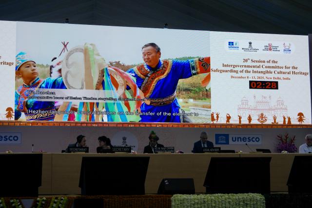 (251211) -- NEW DELHI, Dec. 11, 2025 (Xinhua) -- A video on the protection achievements of China's "Hezhen Yimakan storytelling" is played during the 20th regular session of the Intergovernmental Committee for the Safeguarding of the Intangible Cultural Heritage in New Delhi, India, Dec. 11, 2025. The Intergovernmental Committee for the Safeguarding of the Intangible Cultural Heritage at its 20th regular session decided to transfer China's "Hezhen Yimakan storytelling" from the List of Intangible Cultural Heritage in Need of Urgent Safeguarding to the Representative List of the Intangible Cultural Heritage of Humanity. 
   At the same time, based on the effectiveness of the protection of this heritage project, the committee decided to include the safeguarding program for Hezhen Yimakan storytelling in the Register of Good Safeguarding Practices. (Xinhua/Wu Yue)