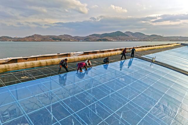 (251211) -- BEIJING, Dec. 11, 2025 (Xinhua) -- A drone photo shows farmers renewing plastic film for cherry greenhouses in Fushan District of Yantai, east China's Shandong Province, Dec. 11, 2025.
  The National Meteorological Center on Wednesday issued a blue alert for a cold wave and a separate blue alert for strong winds, forecasting a widespread drop in temperatures and the first large-scale snowfall this winter across northern China over the next few days. (Photo by Sun Wentan/Xinhua)