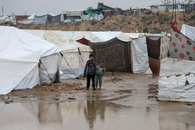 (251211) -- GAZA, Dec. 11, 2025 (Xinhua) -- Displaced Palestinian children stand outside during a rain in the Zeitoun neighborhood, southeast of Gaza City, on Dec. 11, 2025. Heavy winter rains and high winds are pounding flimsy temporary shelters of tents and tarps in the Gaza Strip, putting more vulnerable people at risk, UN humanitarians said on Wednesday. (Photo by Rizek Abdeljawad/Xinhua)