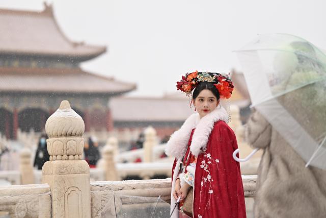 (251212) -- BEIJING, Dec. 12, 2025 (Xinhua) -- A tourist in traditional costumes poses for photos amid snowfall in the Palace Museum in Beijing, China, Dec. 12, 2025. Beijing witnessed its first significant snowfall of this winter season on Friday. (Xinhua/Li Xin)