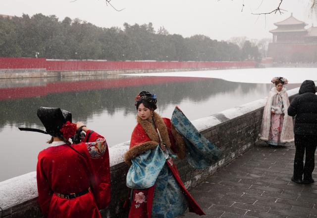 (251212) -- BEIJING, Dec. 12, 2025 (Xinhua) -- Tourists in traditional costumes pose for photos amid snowfall outside the Palace Museum in Beijing, China, Dec. 12, 2025. Beijing witnessed its first significant snowfall of this winter season on Friday. (Xinhua/Yin Dongxun)
