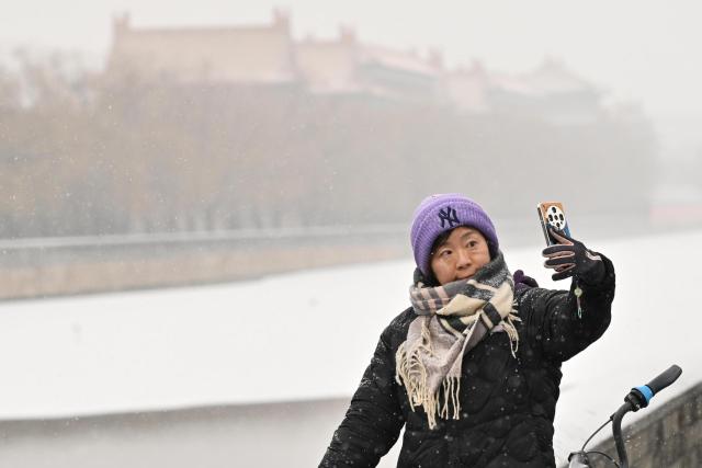 (251212) -- BEIJING, Dec. 12, 2025 (Xinhua) -- A tourist poses for a selfie amid snowfall outside the Palace Museum in Beijing, China, Dec. 12, 2025. Beijing witnessed its first significant snowfall of this winter season on Friday. (Xinhua/Li Xin)