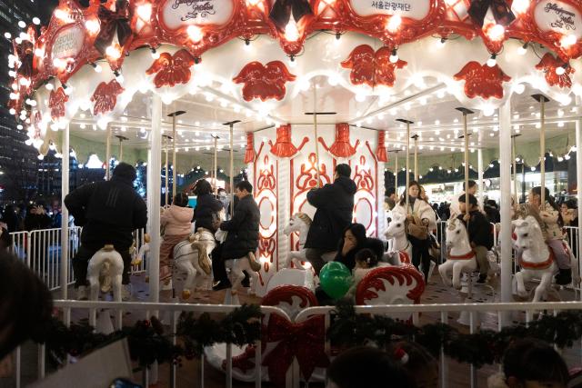 (251212) -- SEOUL, Dec. 12, 2025 (Xinhua) -- People ride a carousel during the 2025 Seoul Winter Festa at the Gwanghwamun Square in Seoul, South Korea, Dec. 12, 2025. (Photo by Jun Hyosang/Xinhua)
