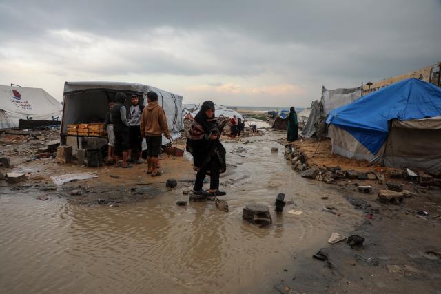 (251212) -- GAZA, Dec. 12, 2025 (Xinhua) -- A Palestinian woman walk in a flooded street after rain in Gaza City, on Dec. 12, 2025. At least 14 people were killed in the Gaza Strip over the past 24 hours as homes collapsed and tents sheltering displaced families were flooded during a powerful winter storm, Gaza's Civil Defense said on Friday. (Photo by Rizek Abdeljawad/Xinhua)