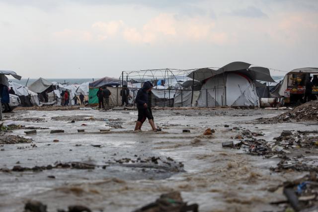 (251212) -- GAZA, Dec. 12, 2025 (Xinhua) -- Palestinians walk in a flooded street after rain in Gaza City, on Dec. 12, 2025. At least 14 people were killed in the Gaza Strip over the past 24 hours as homes collapsed and tents sheltering displaced families were flooded during a powerful winter storm, Gaza's Civil Defense said on Friday. (Photo by Rizek Abdeljawad/Xinhua)