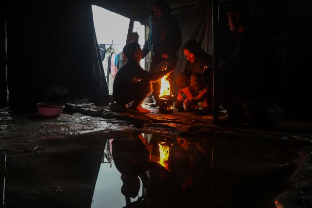 (251212) -- GAZA, Dec. 12, 2025 (Xinhua) -- Palestinians sit around a brazier to stay warm after rain at a temporary shelter in Gaza City, on Dec. 12, 2025. At least 14 people were killed in the Gaza Strip over the past 24 hours as homes collapsed and tents sheltering displaced families were flooded during a powerful winter storm, Gaza's Civil Defense said on Friday. (Photo by Rizek Abdeljawad/Xinhua)