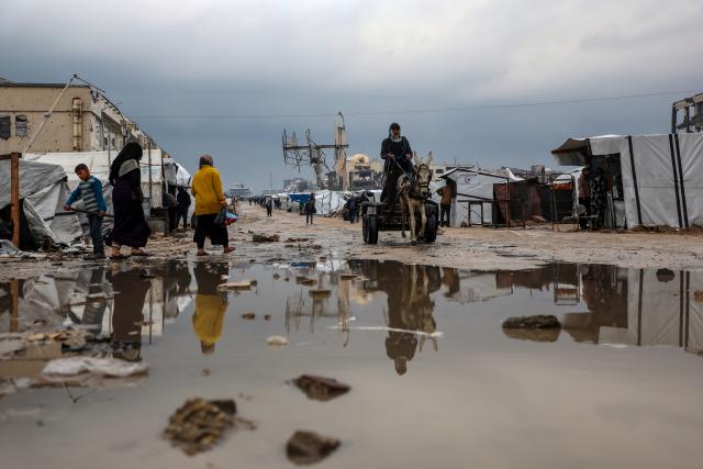 (251212) -- GAZA, Dec. 12, 2025 (Xinhua) -- Palestinians walk in a flooded street after rain in Gaza City, on Dec. 12, 2025. At least 14 people were killed in the Gaza Strip over the past 24 hours as homes collapsed and tents sheltering displaced families were flooded during a powerful winter storm, Gaza's Civil Defense said on Friday. (Photo by Rizek Abdeljawad/Xinhua)