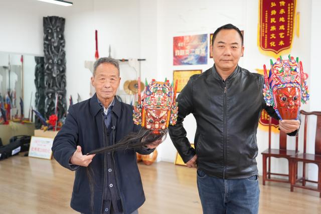 (251213) -- GUIYANG, Dec. 13, 2025 (Xinhua) -- Fang Renliang (L) displays a lacquered wooden mask of Dixi opera in Malu Village of Qiannan Buyi and Miao Autonomous Prefecture in southwest China's Guizhou Province, Nov. 20, 2025. TO GO WITH Across China: "Living-fossil" folk opera connects SW China village to its past (Xinhua)