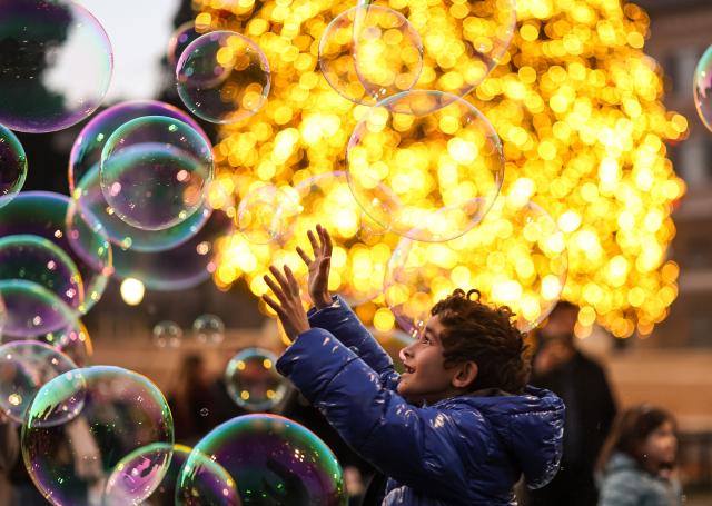(251214) -- ROME, Dec. 14, 2025 (Xinhua) -- A boy plays with bubbles in front of a Christmas tree at Piazza del Popolo in Rome, Italy, Dec. 13, 2025. (Xinhua/Li Jing)