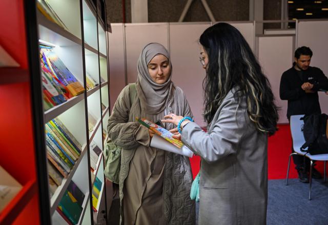 (251214) -- ISTANBUL, Dec. 14, 2025 (Xinhua) -- A Chinese publisher (R) introduces Chinese books to a Turkish reader at the 42nd Istanbul International Book Fair in Istanbul, Türkiye, Dec. 13, 2025. The book fair opened on Saturday in Istanbul, Türkiye's largest city. The Chinese publishing delegation showcased over 700 high-quality books at the book fair, attracting many local readers. (Xinhua/Liu Lei)