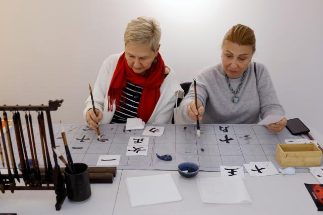 (251214) -- BUCHAREST, Dec. 14, 2025 (Xinhua) -- Guests try Chinese traditional calligraphy during the opening day of the 4th edition of the Buchina Book Fair at the China Cultural Center in Bucharest, Romania, Dec. 13, 2025. Buchina is a book fair dedicated to Chinese literature, culture and art. (Photo by Cristian Cristel/Xinhua)
