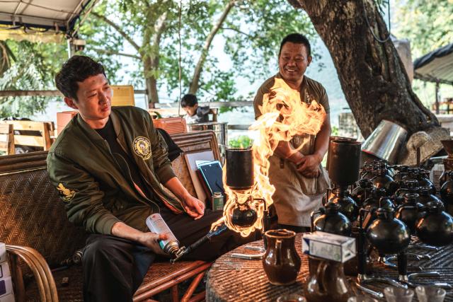 (251214) -- KUNMING, Dec. 14, 2025 (Xinhua) -- Guo Shuai (L), a cafe owner from Benxi in northeast China's Liaoning Province, learns under the instruction of Li Jinhe at the cafe in Mangkuan Township of Baoshan City, southwest China's Yunnan Province, Nov. 15, 2025.
  Mandabatmaz, a Turkish cafe, is located in a small alley beside Istiklal Avenue in Istanbul.
  The owner, Can Ozmen, took over this small coffee shop with a history of nearly sixty years from his parents. To carry on the tradition, he still insists on brewing coffee with copper pots. Ozmen introduced that Turkish coffee should be consumed with coffee grounds, which makes Turkish coffee unique. "Unlike other coffees, which are filtered, Turkish coffee is enjoyed in its entirety," Ozmen explained.
  Turkish coffee has a long history and was inscribed on UNESCO's Representative List of the Intangible Cultural Heritage of Humanity in 2013.
  While in China, a riverside cafe in Yunnan also wins fame among coffee lovers.
  Li Jinhe, 53, has operated his cafe in Mangkuan under Baoshan City in Gaoligong Mountains for 14 years.
  His "flame-brewed coffee", which made by a blowtorch to heat beneath siphon pots, has taken the Internet by storm for its originality, turning his cafe into a viral sensation.
  Tourists said that the coffee shop by the Nujiang River has broken the stereotype of urban coffee, and coffee should be a daily drink integrated into life.
  "I grew up here, and love Gaoligong Mountains," said Li. The Gaoligong Mountains, where fertile soil, ideal temperatures and abundant sunlight situate it within the global coffee-growing belt, boast small-bean coffee. "It is my unwavering commitment to promote local small-bean coffee," added Li.
  Although made by different ways, both Turkish and Chinese coffee tell the story of people's pursuit of life with warmth and aroma. (Xinhua/Wang Guansen)